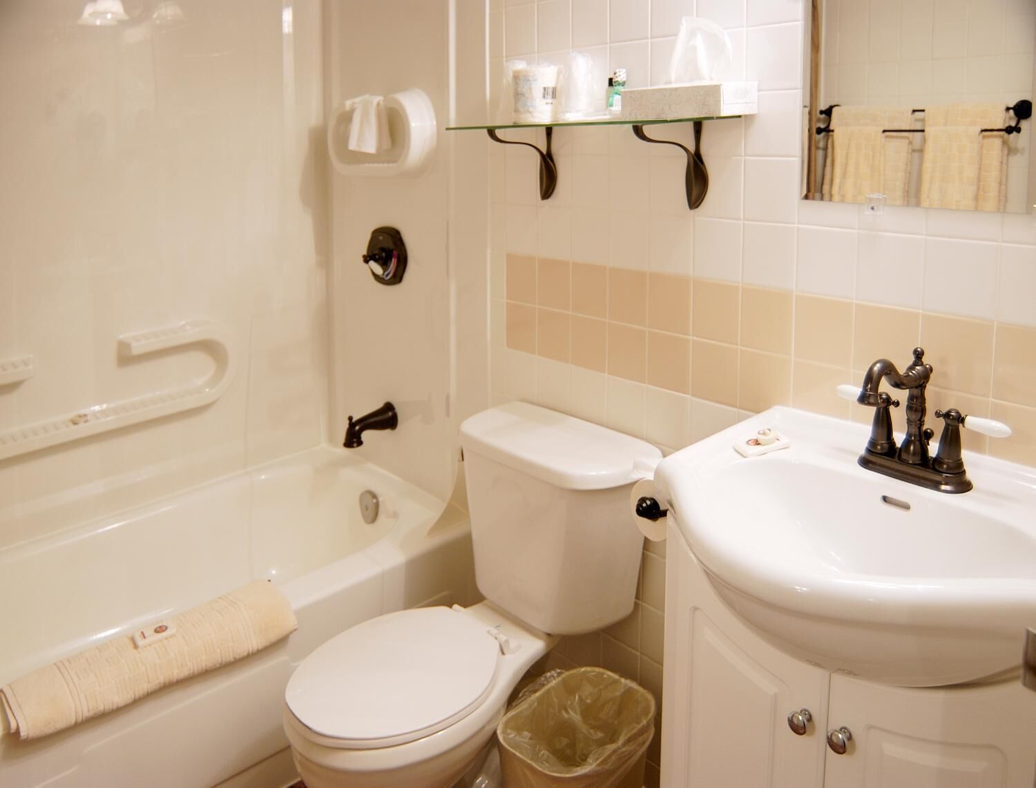 A bathroom with a bathtub, toilet, and sink. There is a towel rack above the sink and a trash can next to the toilet.