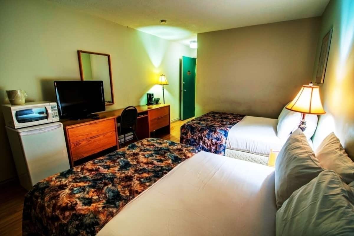 Ein Hotelzimmer mit zwei Betten, einem Schreibtisch, einem Fernseher, einer Mikrowelle und einer Lampe.