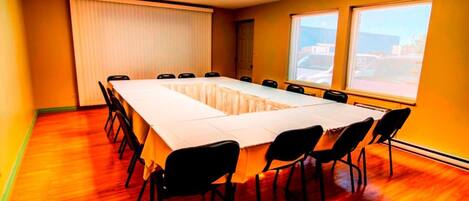 Un salón de conferencias con una larga mesa, sillas, una pantalla de proyector y ventanas.