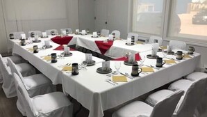 A conference room with a long table, white chairs, and a red runner. - Wescana Inn (The Pas)