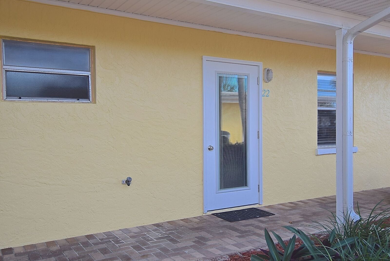 A yellow building with a white door, a small window, and a number '22' on the wall.