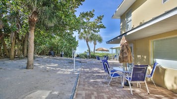 Eine Terrasse mit blauen Stühlen und einem Tisch, eine Palme und ein Gebäude mit einem grünen Rollo.