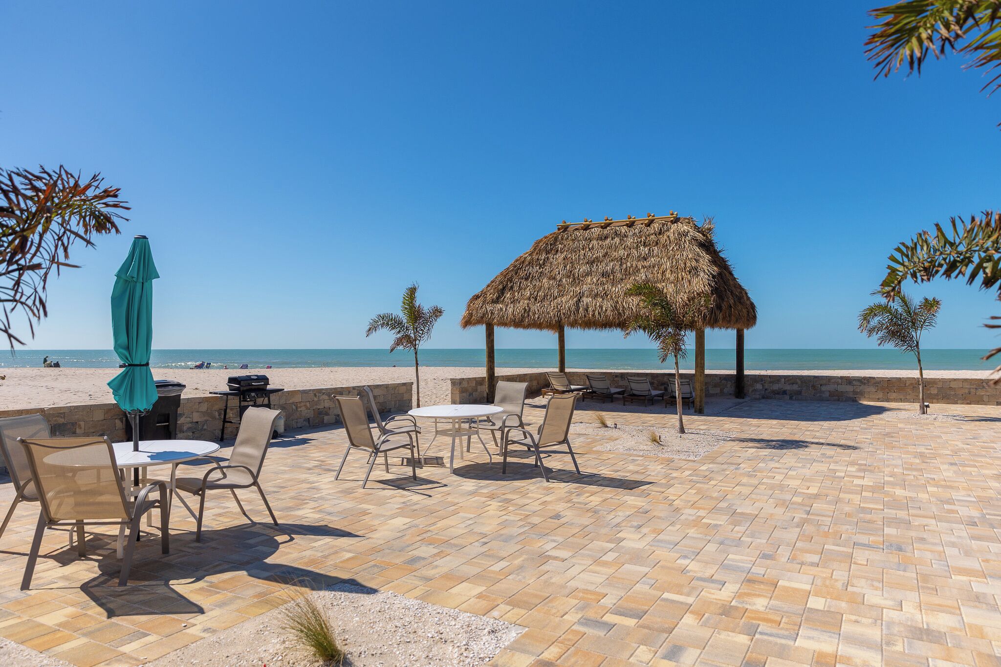 A beachside patio with a thatched-roof structure, outdoor seating, and a view of the beach.