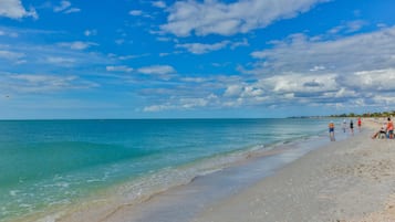 A beach with clear turquoise water, a sandy shore, and a few people walking along the beach.