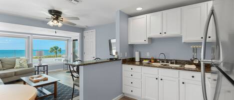 A modern kitchen with white cabinets, a stainless steel refrigerator, and a view of the ocean.