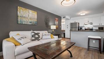 A modern living room with a white sofa, a coffee table, and a kitchen in the background.