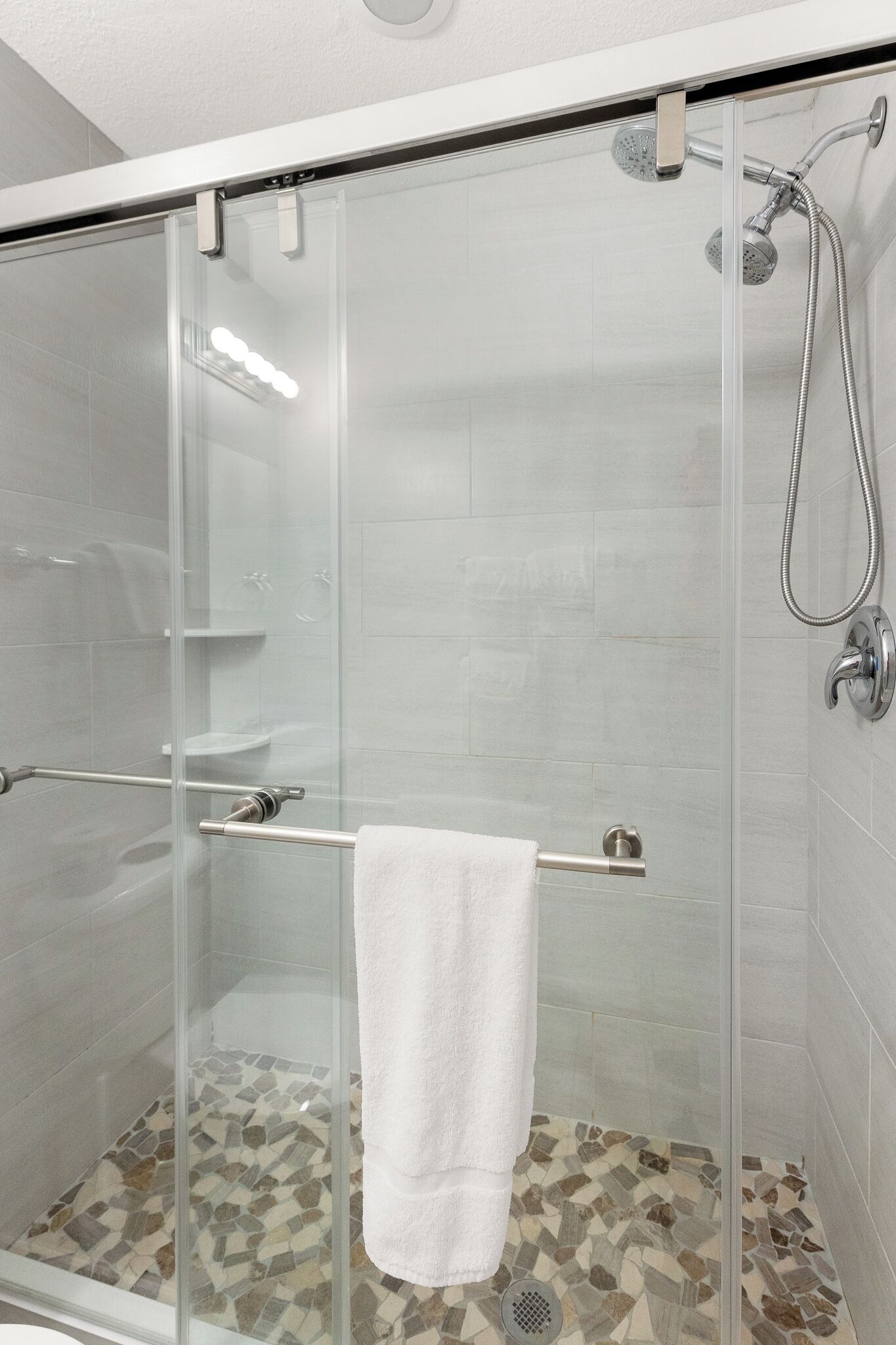 Une douche fermée par des parois de verre, avec une serviette blanche suspendue à une barre métallique, des murs carrelés et un sol à motifs.