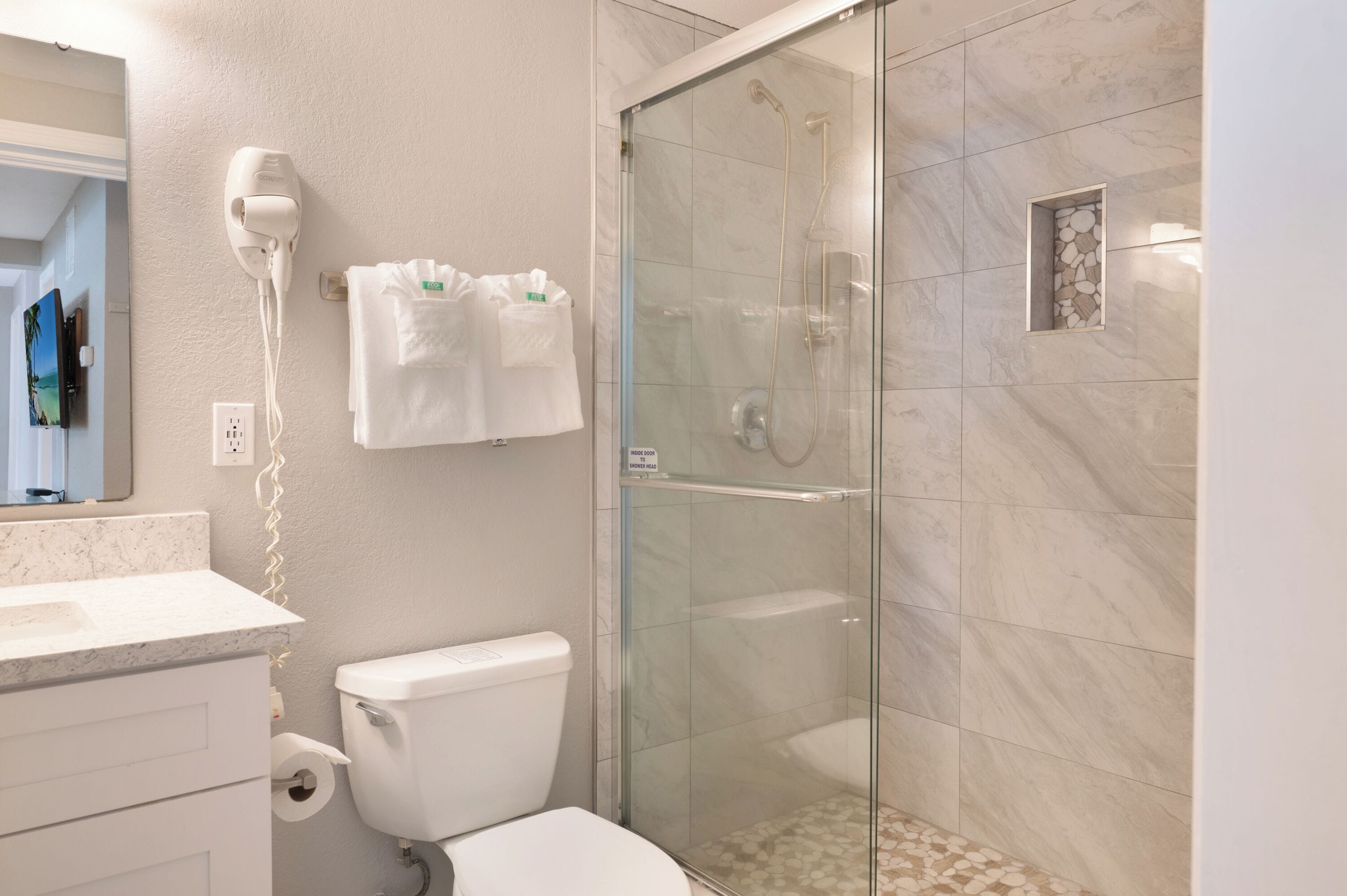 A modern bathroom with a glass-enclosed shower, a toilet, a hairdryer, and a towel rack.