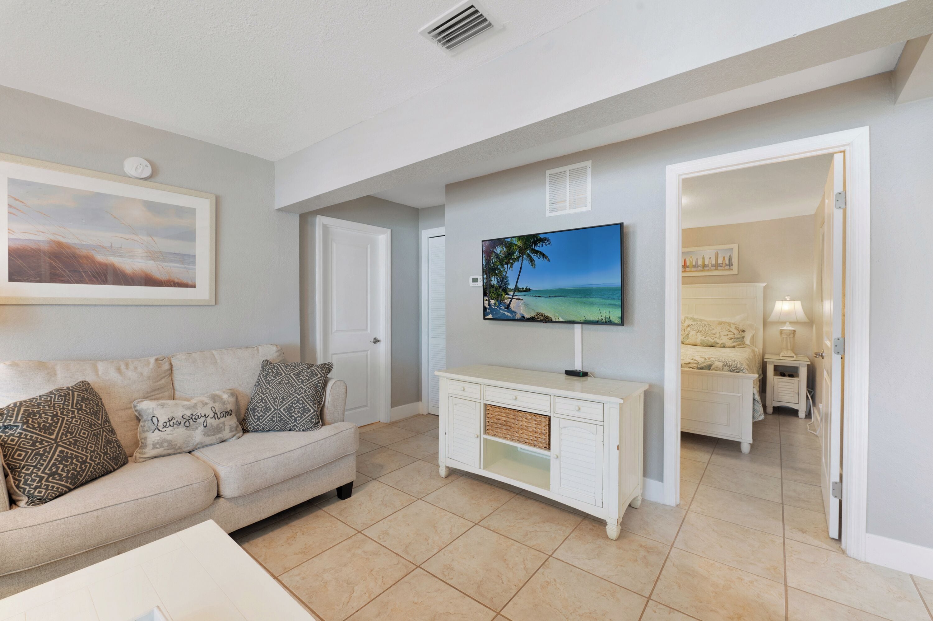 A living room with a beige sofa, a flat-screen TV, and a white cabinet.