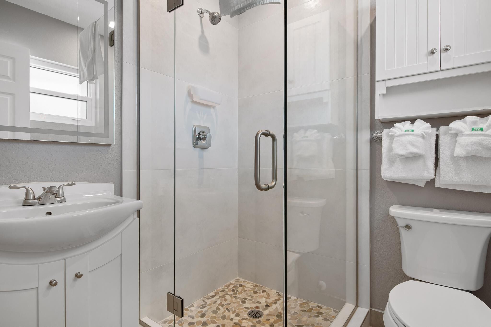 Un baño con ducha de vidrio, lavamanos blanco y retrete.