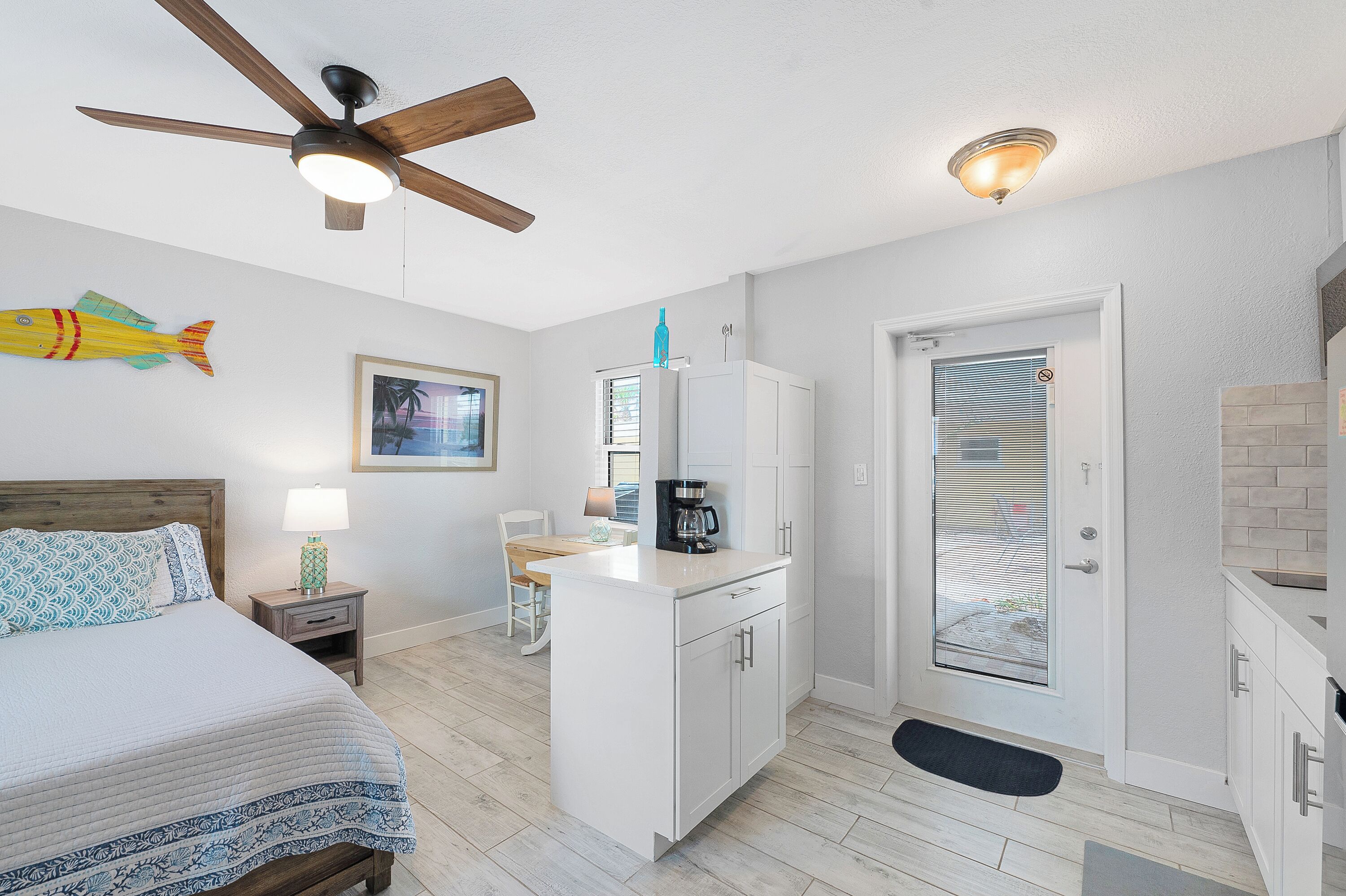 Une chambre à coucher comprenant un lit, une table de chevet, une lampe, un ventilateur de plafond, une petite table avec une lampe et un tableau accroché au mur.