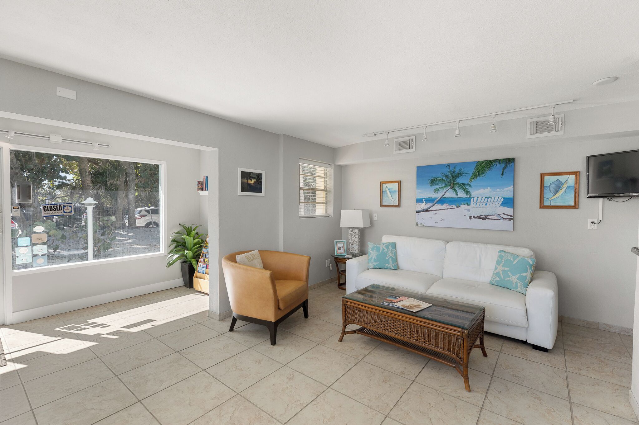 A living room with a white sofa, a brown armchair, a coffee table, and a large window with a view of the street.