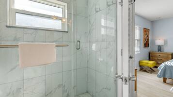 Un baño con cabina de ducha de vidrio, una toalla colgada en un perchero y una ventana sobre la ducha.