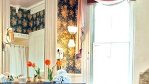 Una habitación con un tocador blanco, un espejo y una ventana con cortina rosa.