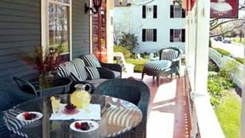 A covered porch with wicker furniture, a glass table, and a red awning.