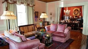 Un salón tradicional con un sofá, sillones y una mesa de centro. Se puede ver un comedor a través de una puerta abierta.