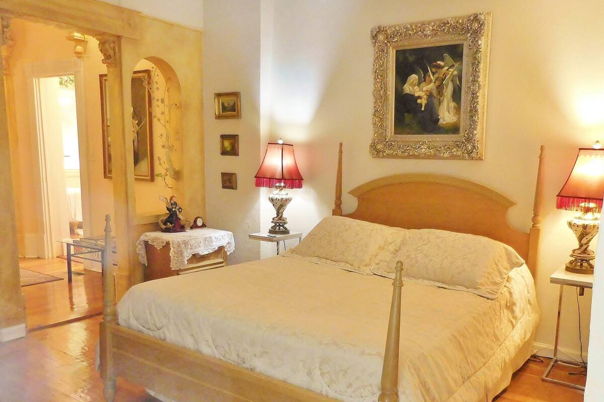 A bedroom with a large bed, two bedside tables with lamps, a wooden headboard, and a painting on the wall.