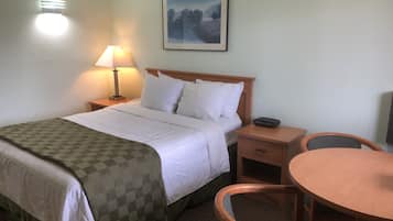 Une chambre d’hôtel avec un lit, une lampe de chevet, un tableau encadré au mur, une petite table avec une chaise et une table de chevet avec un téléphone.
