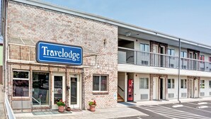 Un hôtel Travelodge avec une façade en briques, un balcon à l’étage supérieur et un parking à l’avant.