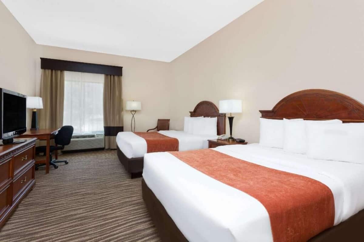 Hotelkamer met twee bedden, een bureau met een televisie, een stoel en een raam met gordijnen.