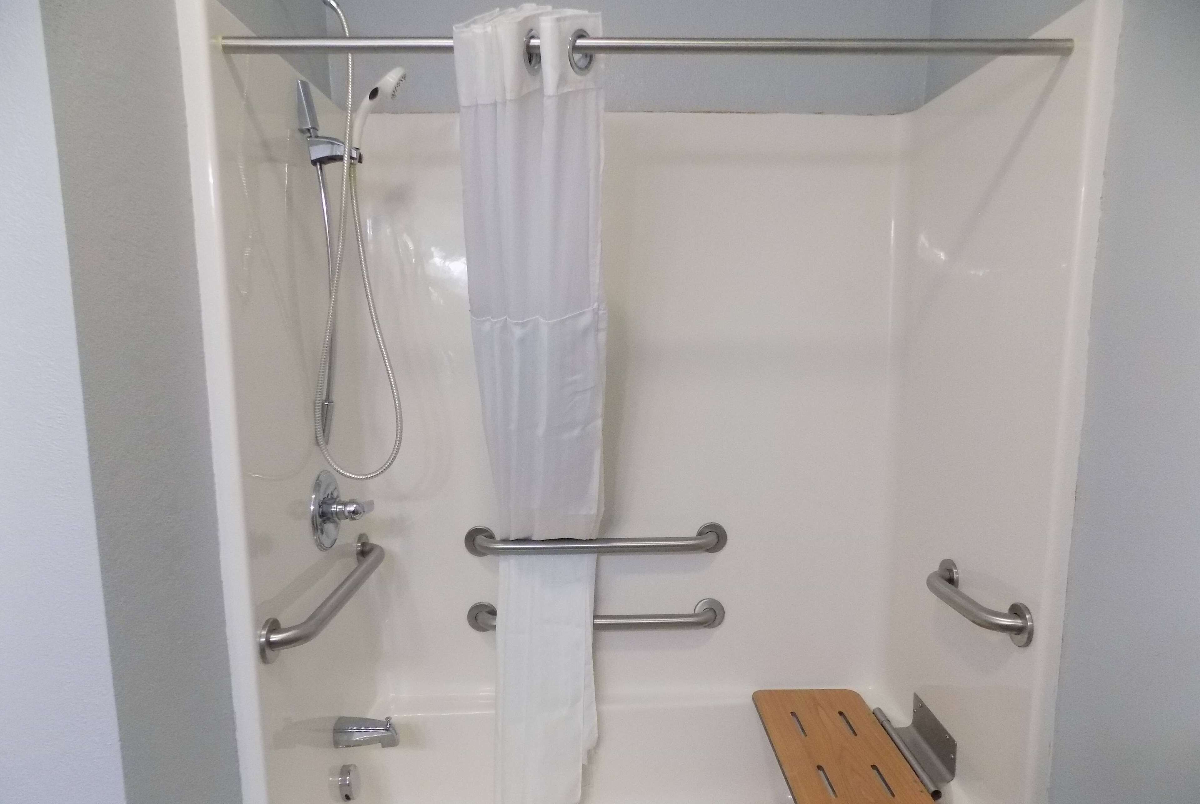 Zona de ducha con cortina blanca, barras de apoyo y un escalón de madera.