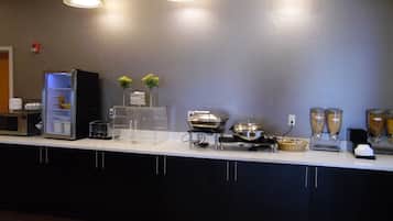 A buffet setup with a microwave, a refrigerator, and various food containers on a counter.