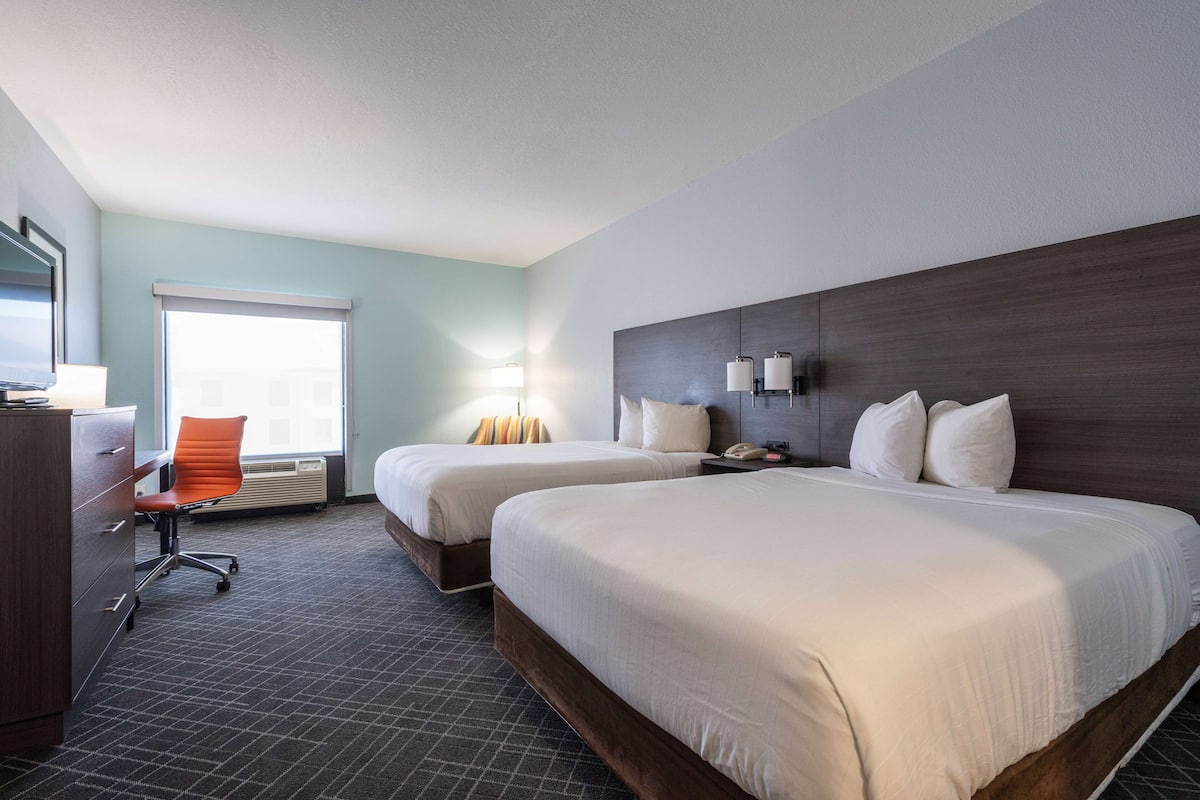 Een hotelkamer met twee bedden, een bureau, een stoel, een lamp en een raam.