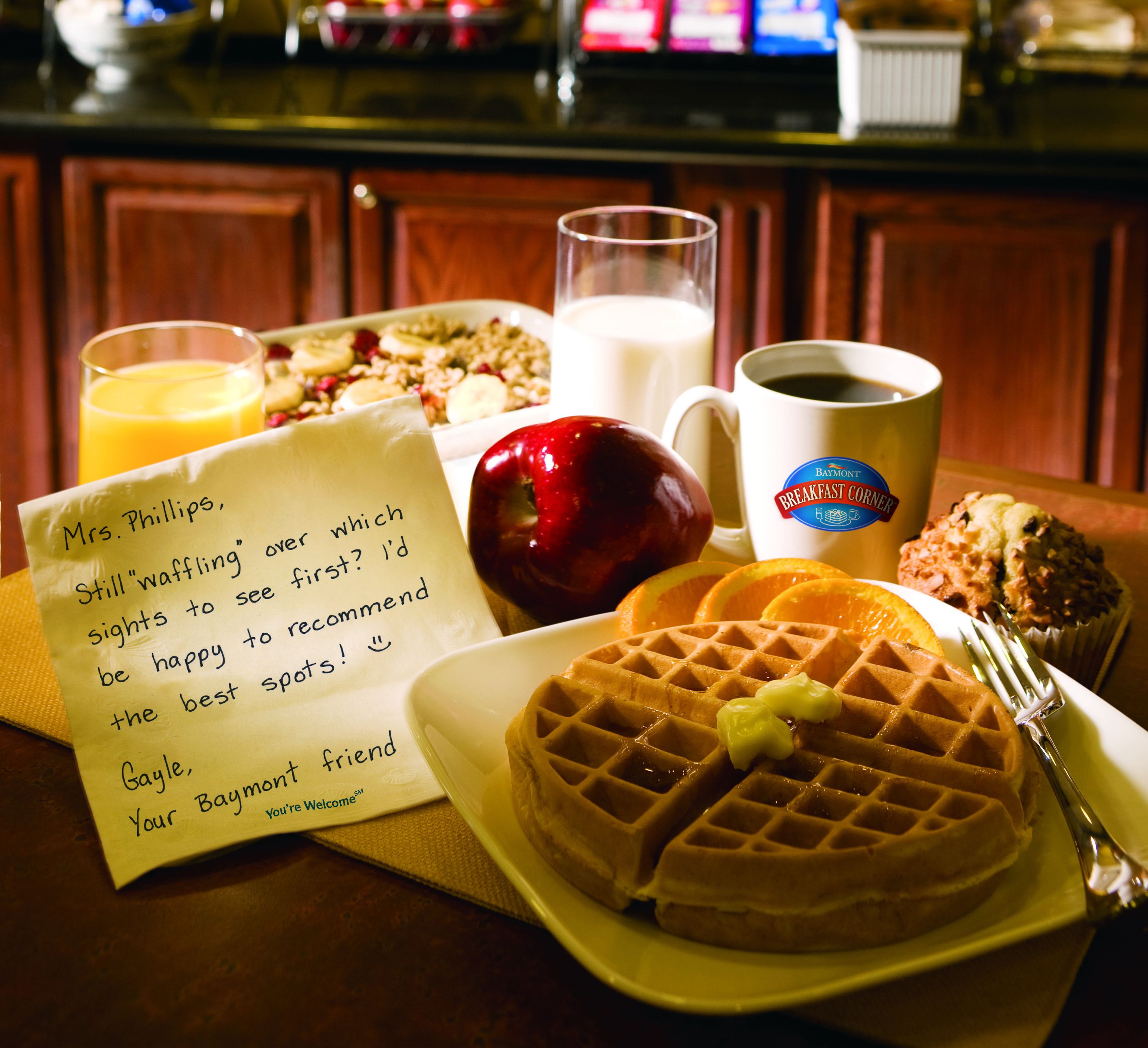 A breakfast setting with waffles, apple, orange slices, coffee, and a note.