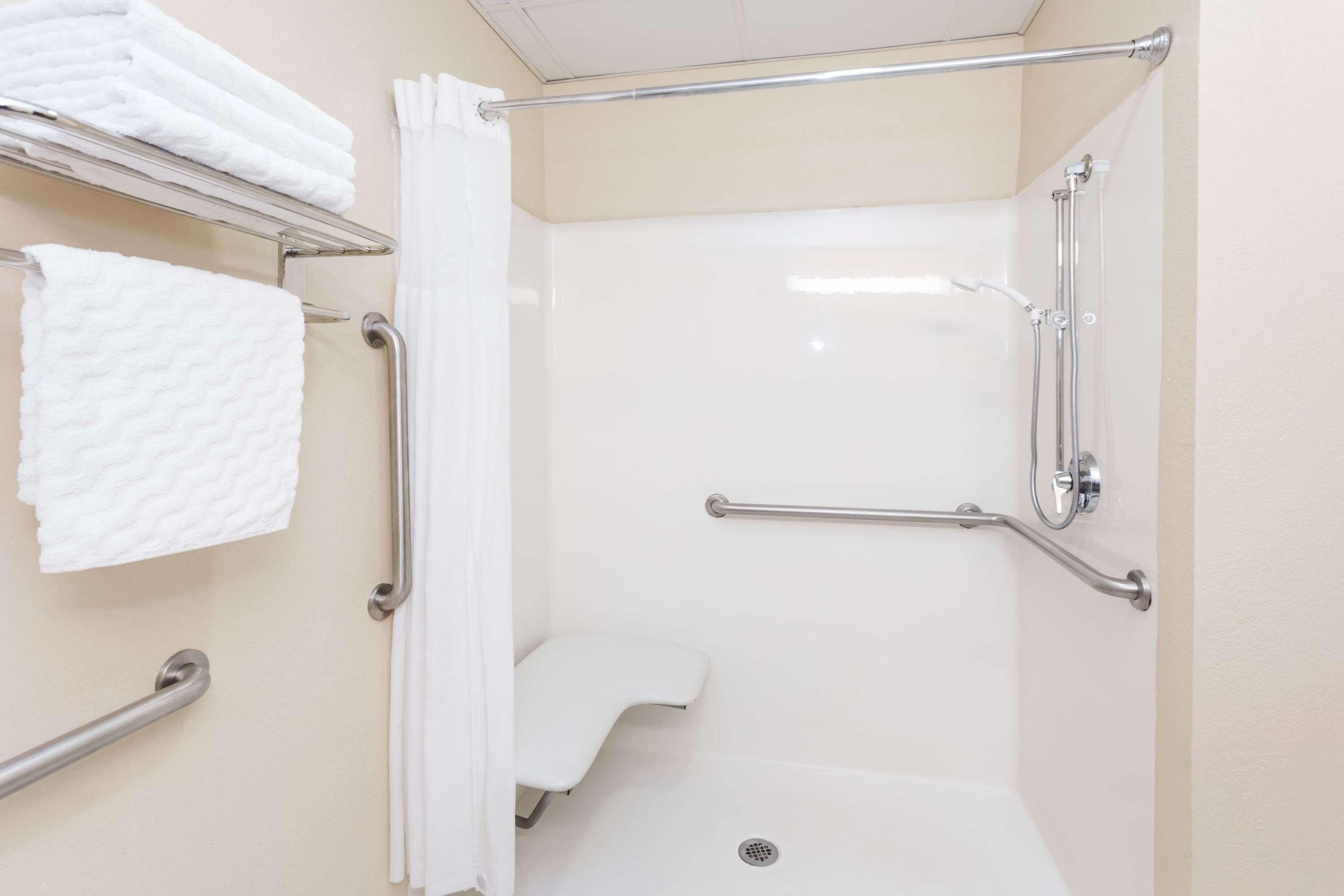 A handicap-accessible shower area with grab bars, a white bathtub, and a towel rack with folded towels.