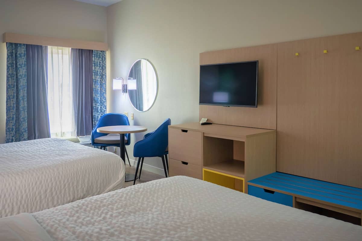 Une chambre d’hôtel avec deux lits, un bureau, une chaise, une télévision et un miroir.