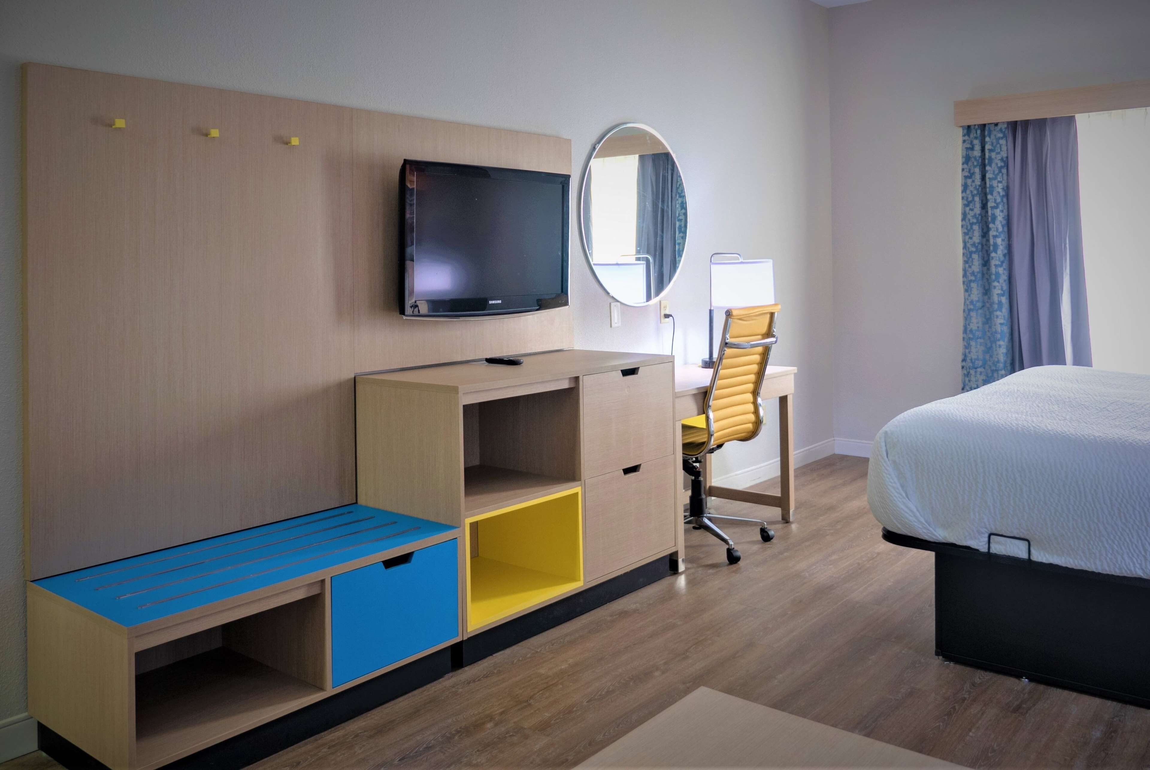 A hotel room with a bed, a desk with a chair, a TV, a mirror, and a wardrobe.