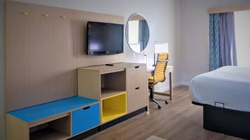 A hotel room with a bed, a desk with a chair, a TV, a mirror, and a wardrobe.