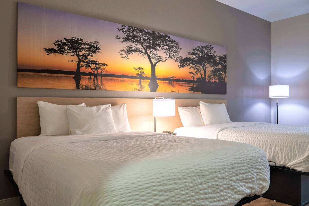 Une chambre d’hôtel avec deux lits, une grande peinture représentant un coucher de soleil sur l’eau et une table de chevet avec une lampe.