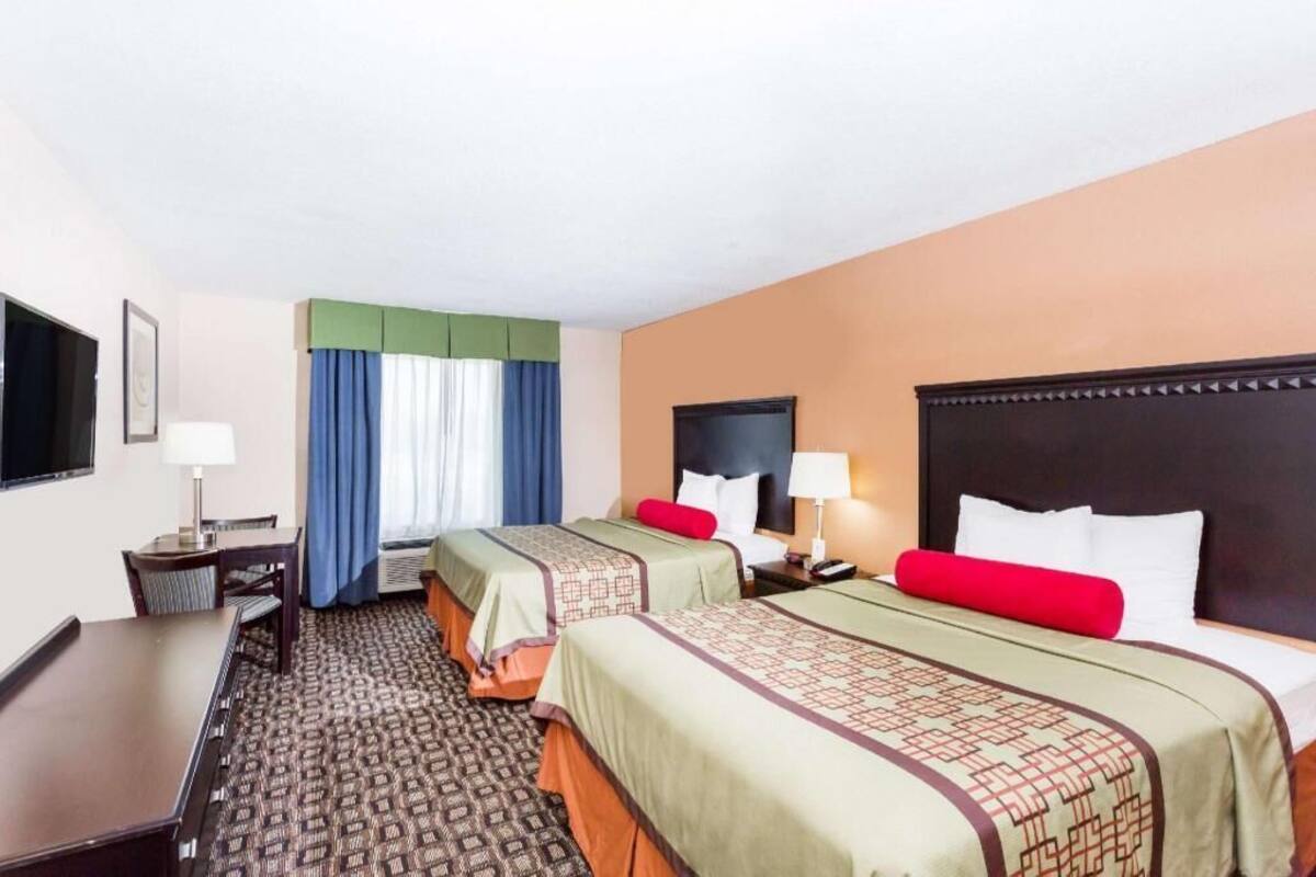 Ein Hotelzimmer mit zwei Betten, einem Schreibtisch, einem Stuhl, einem Fernseher und einem Fenster mit Vorhängen.