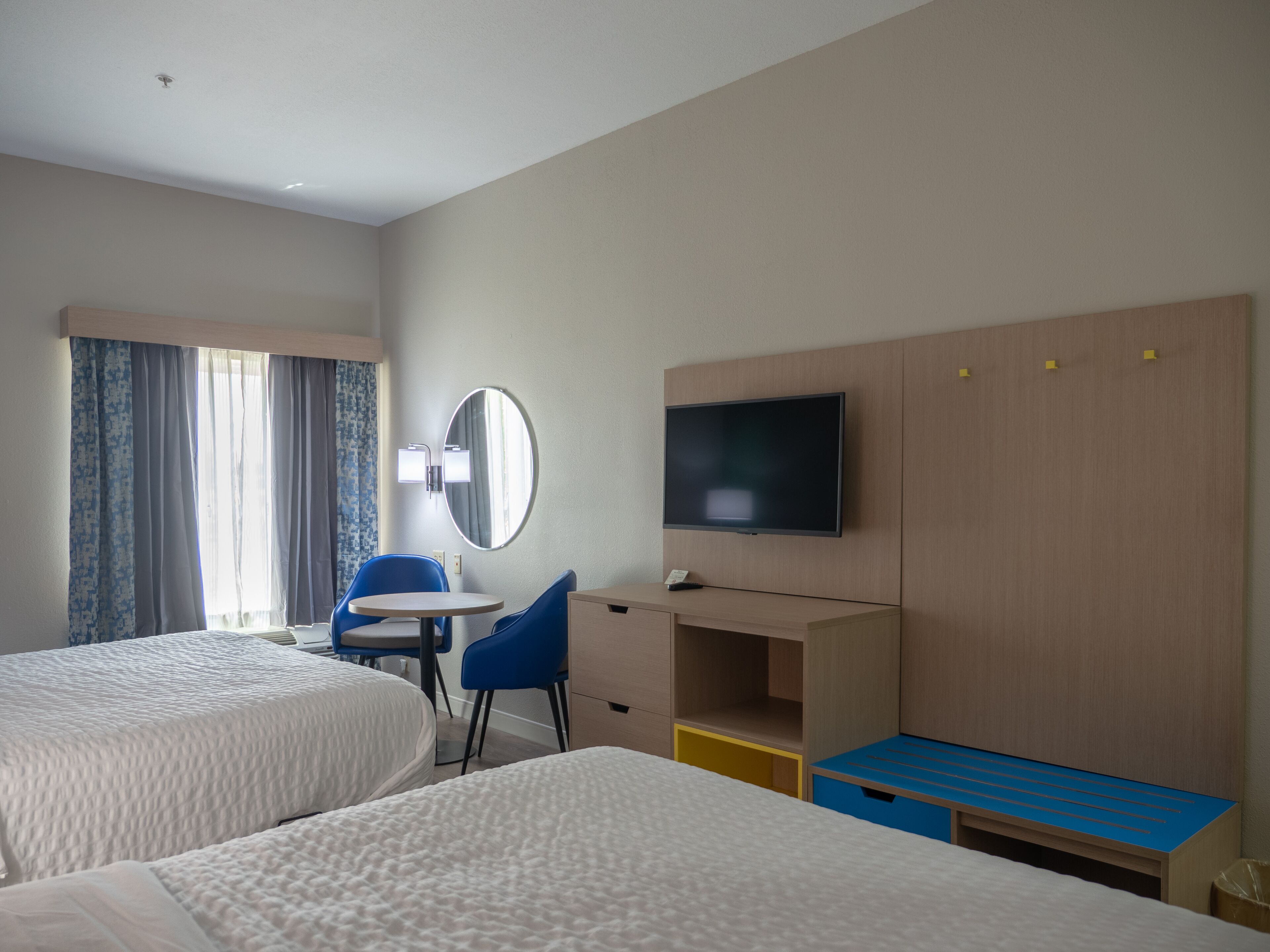 A hotel room with two beds, a desk, a chair, a television, and a mirror.