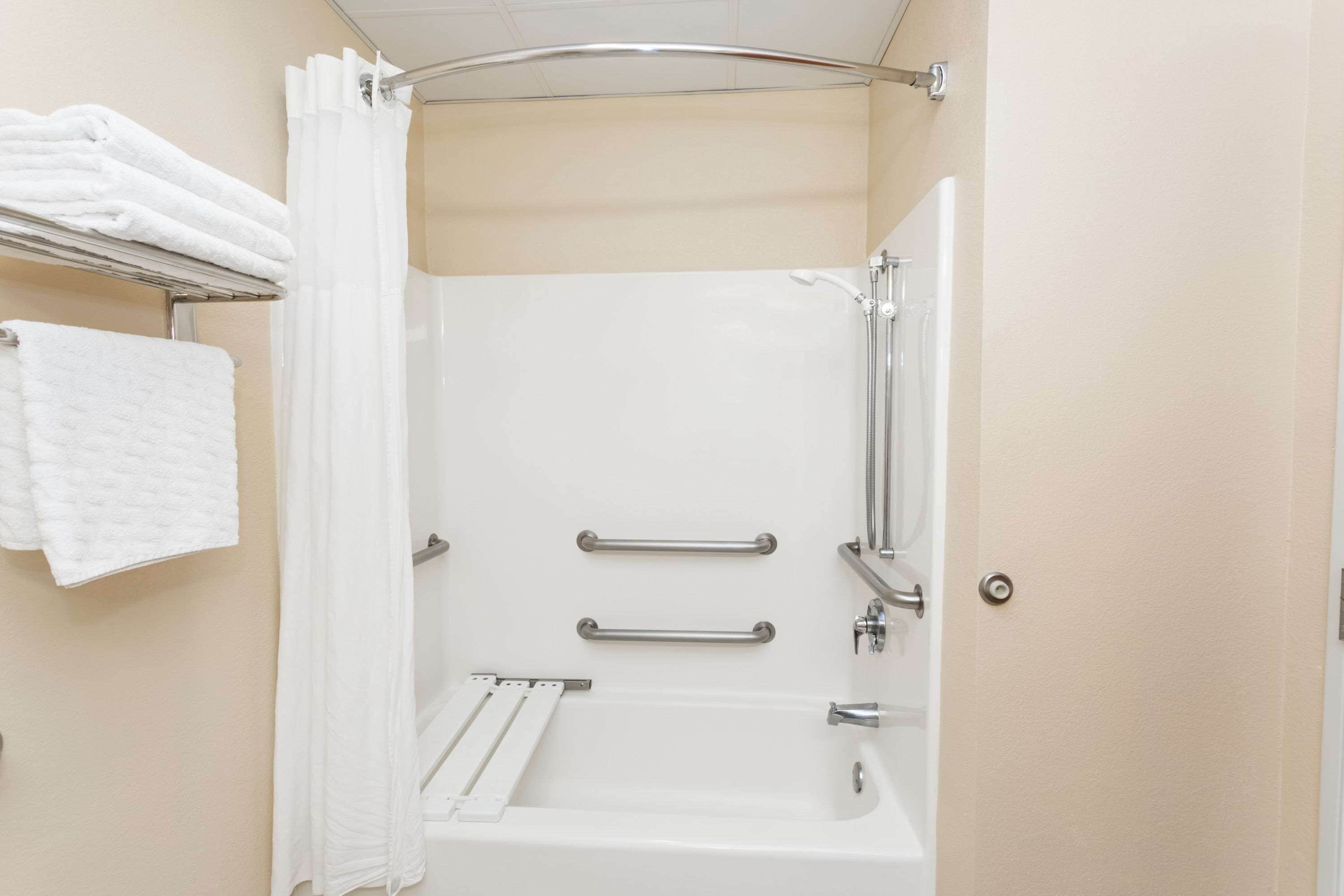 A bathroom with a white bathtub, two grab bars, a shower curtain, and a towel rack with folded towels.