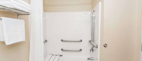 A bathroom with a white bathtub, two grab bars, a shower curtain, and a towel rack with folded towels.