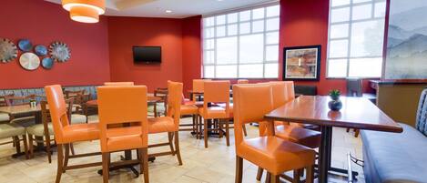 A restaurant with orange chairs, a wooden table, and a large window with a mountain view.