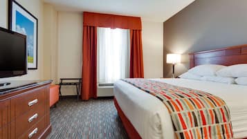 A hotel room with a bed, a TV, a desk, and a window with curtains.