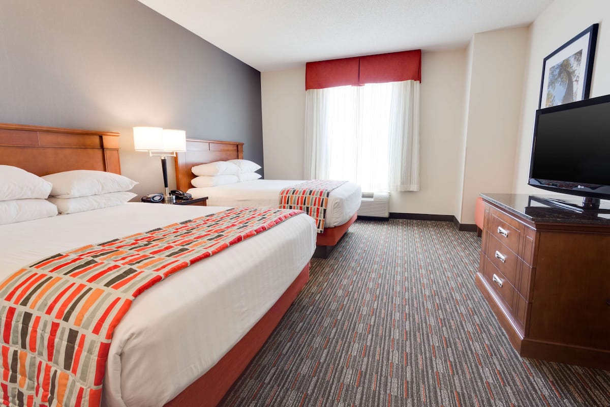 Une chambre d’hôtel avec deux lits, une télévision, un bureau et une fenêtre avec des rideaux.