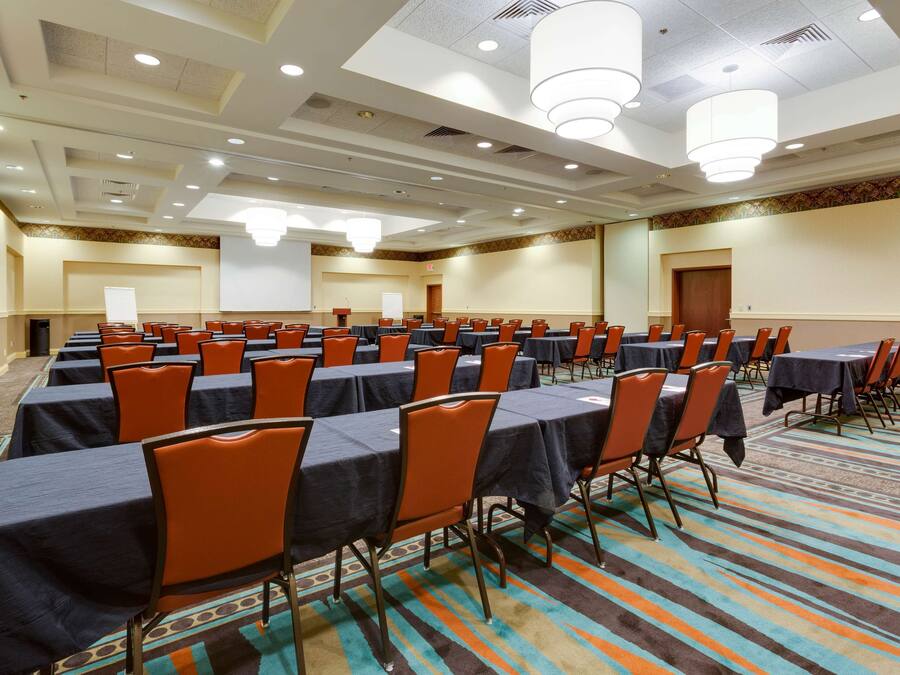A conference room with rows of tables and chairs, a projector screen, and a carpeted floor.