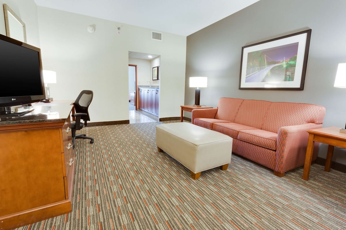 Une chambre d’hôtel équipée d’un téléviseur à écran plat, d’un bureau avec des tiroirs, d’un canapé confortable, d’une petite table et d’un tableau encadré au mur.