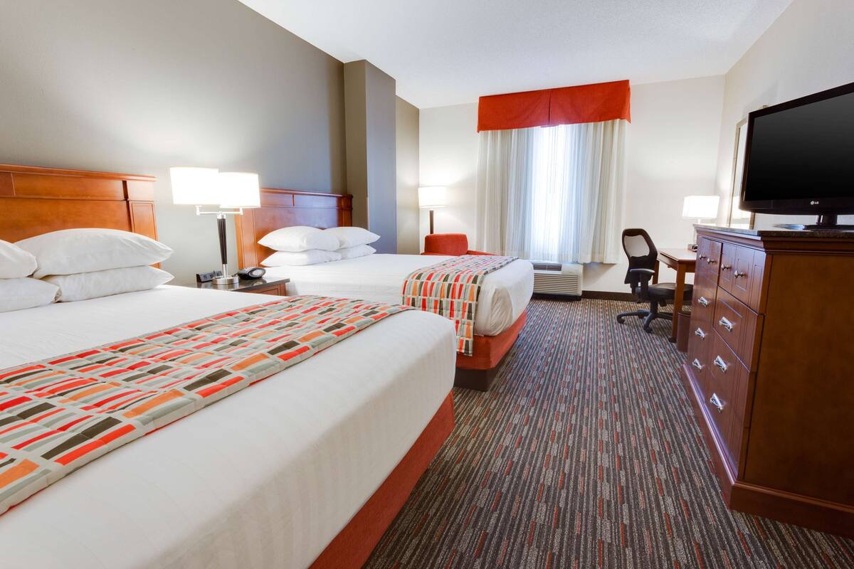 Une chambre d’hôtel avec deux lits, un bureau, une chaise, une télévision et une commode.