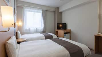 A hotel room with two beds, a television on a wooden stand, a desk with a phone, and a window with curtains.