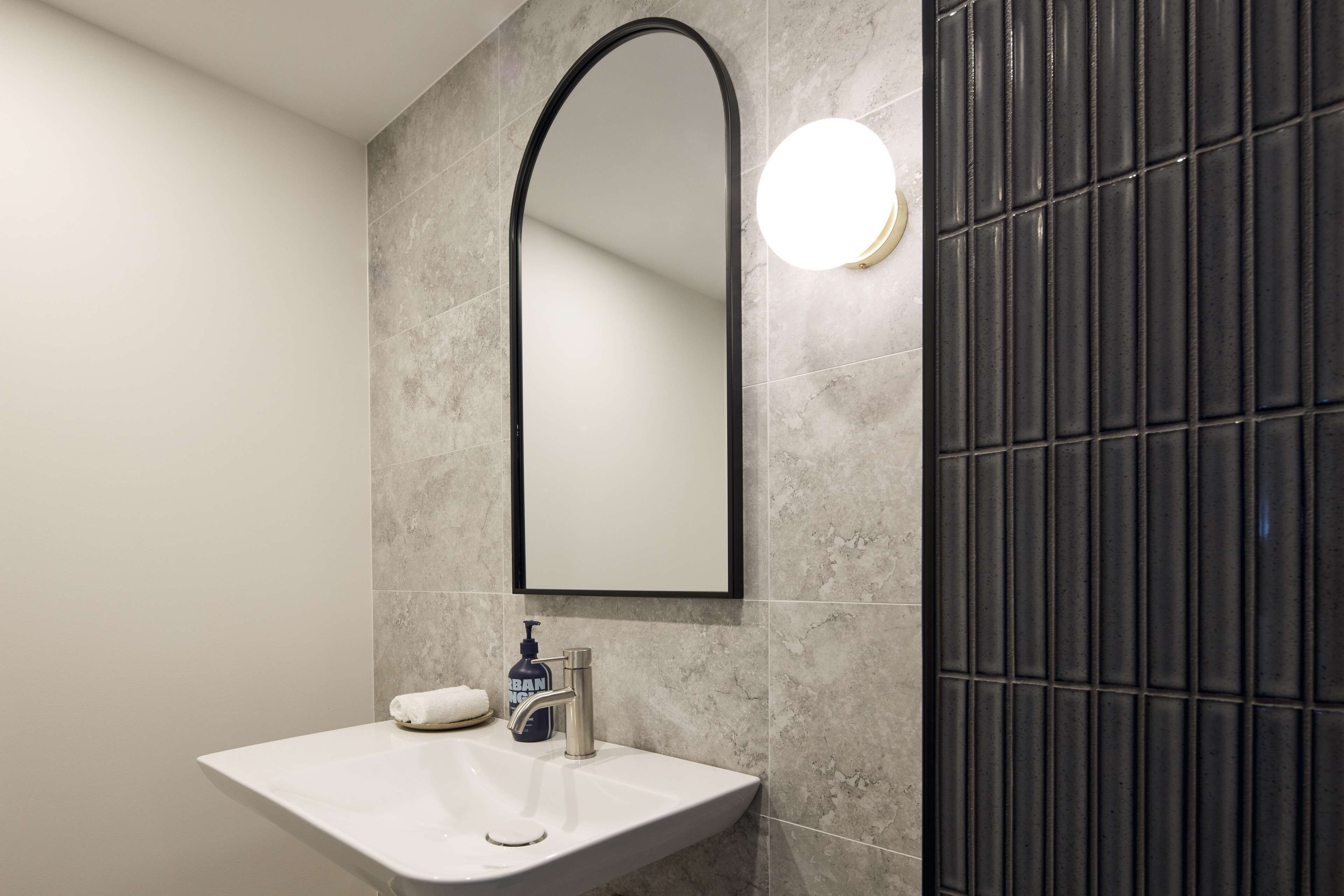 A bathroom with a white sink, a mirror, and a soap dispenser.