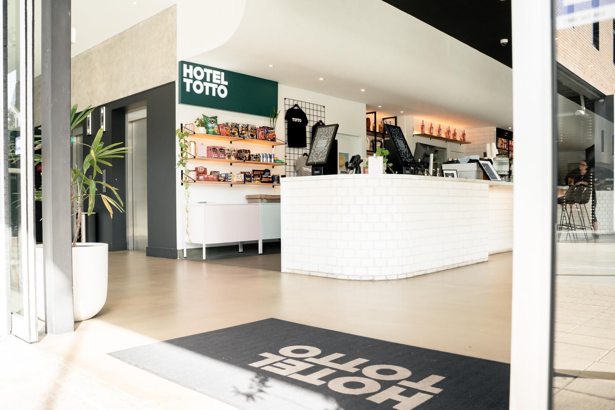 A hotel lobby with a reception desk, a sign reading "HOTEL TOTO," and a doormat with "HOTEL TOTO" on it.