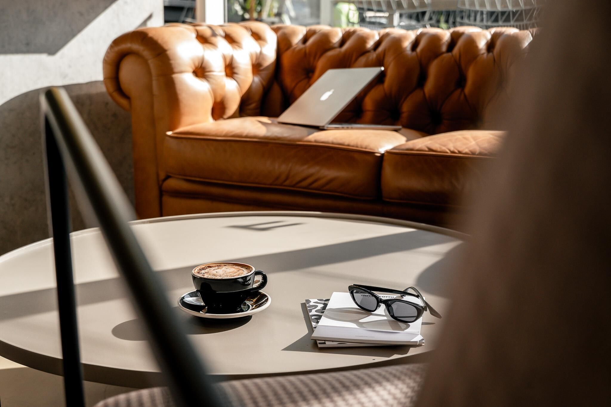 Une table ronde avec un ordinateur portable, une tasse de café et une paire de lunettes.