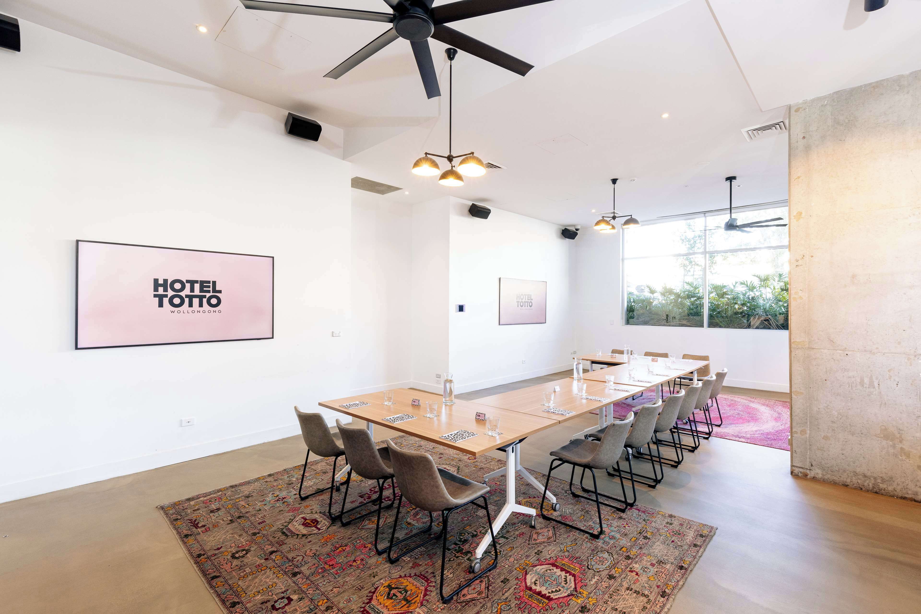 A modern conference room with a long table, chairs, and ceiling fans.