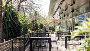 An outdoor cafe area with tables and chairs, surrounded by greenery and a modern building facade. - Hotel TOTTO Wollongong (Wollongong)