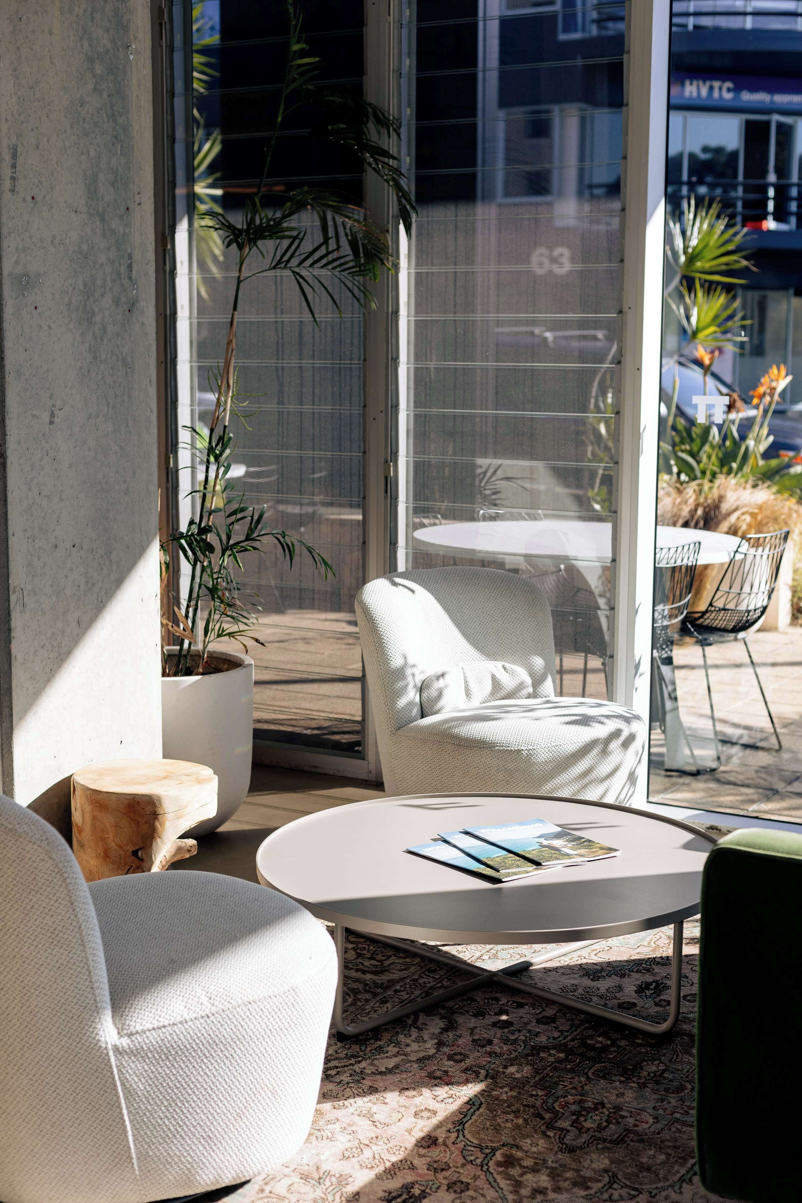 A modern indoor seating area with a round table, white chairs, and a large window with a view of the street.